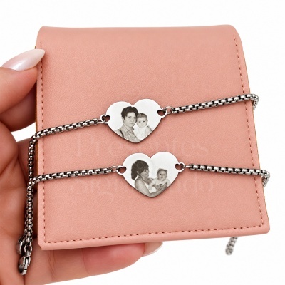 Duas pulseiras com pendentes de coração em metal prateado gravados com fotos, sobre carteira rosa segurada por mão