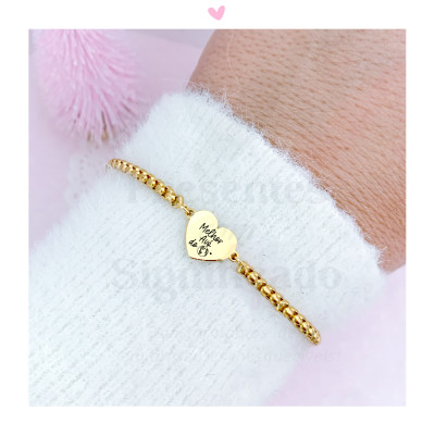 Pulseira dourada com coração gravado 'Melhor tia do MS', pulso com manga branca felpuda