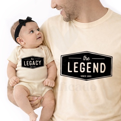 Homem com camisola bege e bebé com body bege e fita preta na cabeça, ambos com texto estampado preto.