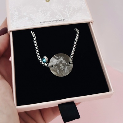 Colar de corrente metálica prateada com pendente circular gravado e pendente azul numa caixa de oferta