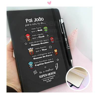 Caderno preto personalizado com texto em português e ilustrações de super-heróis acompanhado por caneta preta