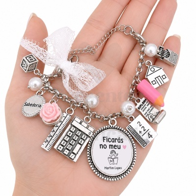 Pulseira prateada com vários pendentes alusivos à escola e educação, com um laço branco