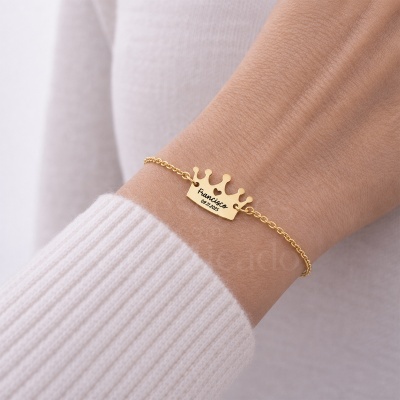 Pulseira dourada com pendente de coroa gravado no pulso