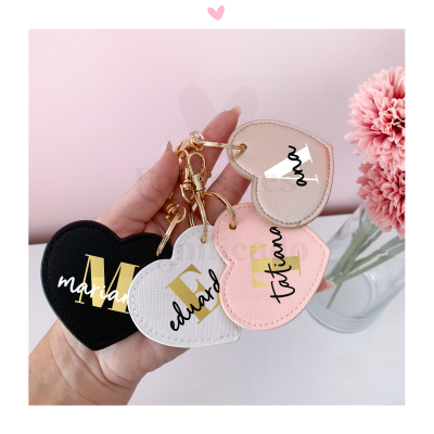 Porta-chaves coração em preto, branco e rosa com nomes personalizados, junto a flor rosa em vaso
