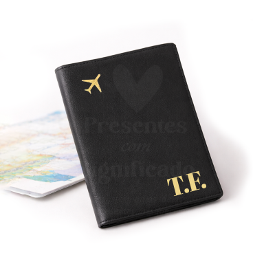 Porta-passaporte preto com avião e iniciais T.F. douradas, pousado sobre superfície branca com mapa ao fundo.