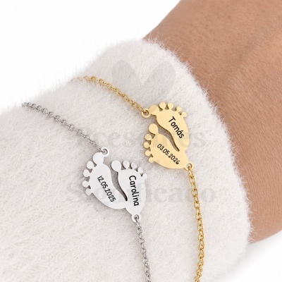 Pulseiras com pendentes em forma de pegadas de bebé, metal dourado e prateado, gravadas com nomes e datas, usadas num pulso com manga branca