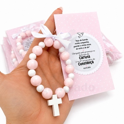 Pulseira rosa e branca com crucifixo e cartão cor de rosa com mensagem de batizado