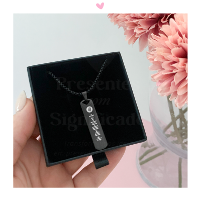 Colar preto com pendente retangular e padrão branco em caixa preta com flores cor-de-rosa ao lado