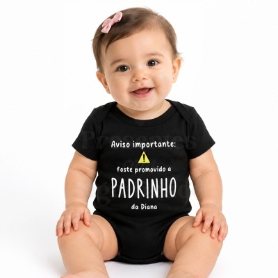 Bebé sorridente com body preto com texto personalizado e laço rosa no cabelo sentado sobre fundo branco.