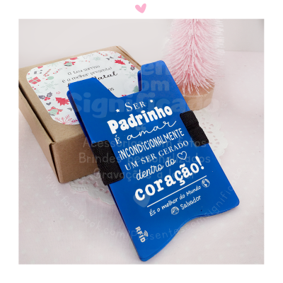 Suporte de cartão azul com texto em branco sobre superfície branca com caixa castanha e árvore decorativa rosa ao fundo