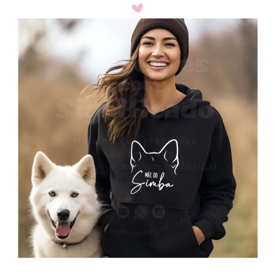 Mulher sorridente com camisola preta 'MÃE DO Simba' e cão branco ao lado, em ambiente exterior