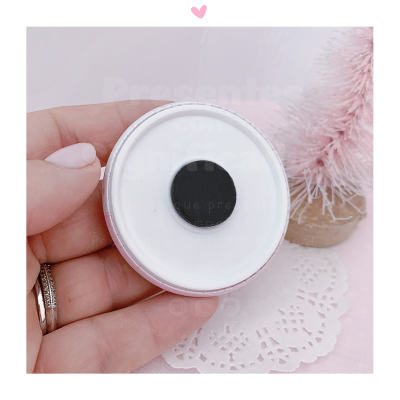 Vela branca redonda com pavio preto segurada por uma mão, com pinheiro rosa ao fundo