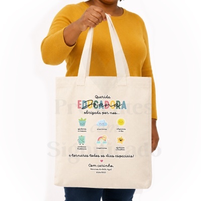 Sacola de tecido com texto e ilustrações coloridas, segurada por pessoa com suéter amarelo