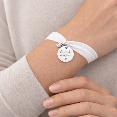 Pulseira branca com pendente redondo prateado com texto e pendente com pedra