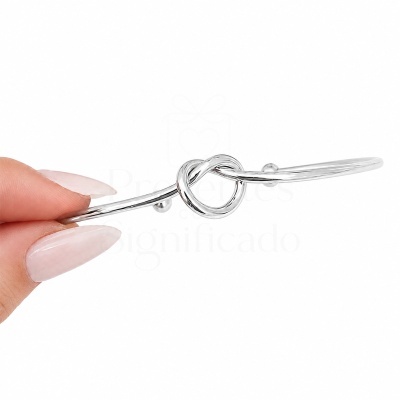 Pulseira prateada com nó no centro segurada por mão feminina