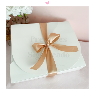 Caixa branca com laço dourado e flores brancas ao lado