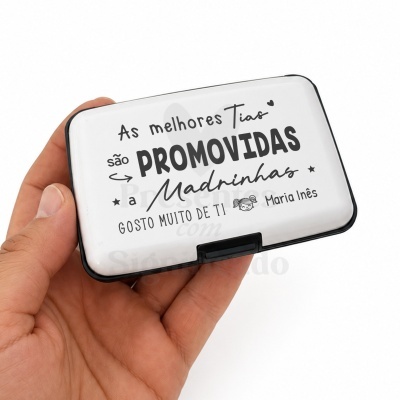 Estojo retangular branco com texto preto sobre promoção de tias a madrinhas