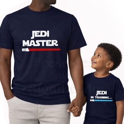 Duas pessoas vestem t-shirts azuis escuras com texto JEDI MASTER e JEDI IN TRAINING... e sabres de luz, uma vermelha e outra azul.