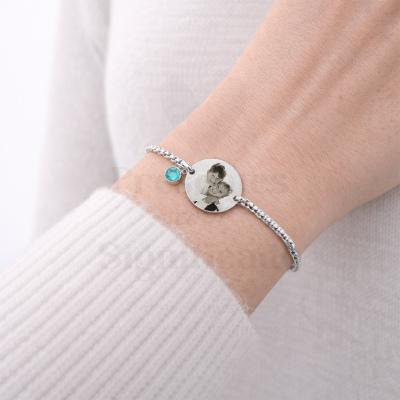 Pulseira prateada com pendente redondo e pedra azul no pulso