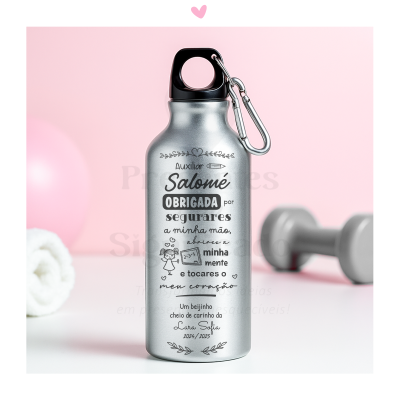 Garrafa metálica prateada com texto personalizado e mosquetão sobre superfície branca e fundo rosa