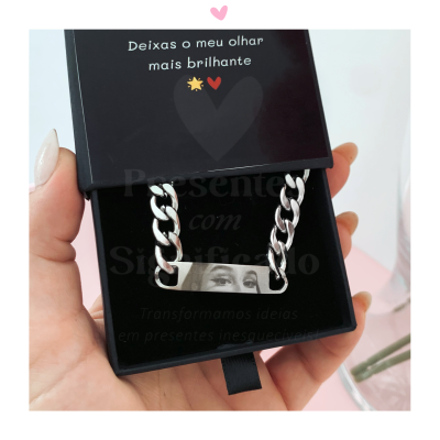Pulseira metálica prateada numa caixa preta com texto inspiracional em português.