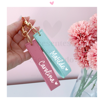 Porta-chaves de couro rosa e azul com nomes personalizados, diante de flores cor de rosa