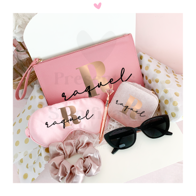 Acessórios femininos rosa claros com letras douradas e nome raquel, óculos de sol pretos, elástico de cabelo, sobre fundo claro com padrão dourado.