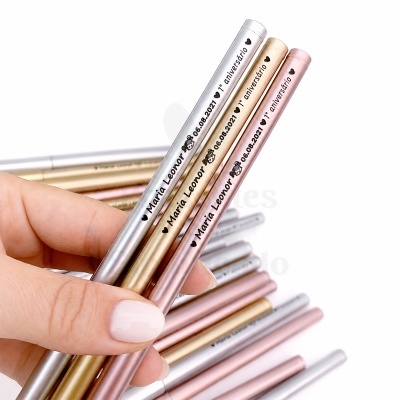 Três lápis metálicos personalizados com nome e data, com cores prateado, dourado e rosa, segurados por mão feminina.