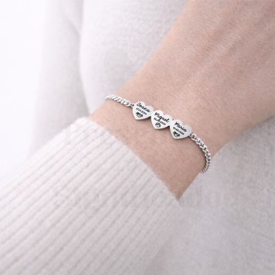 Pulseira prateada com três corações gravados no pulso de pessoa com camisola branca.