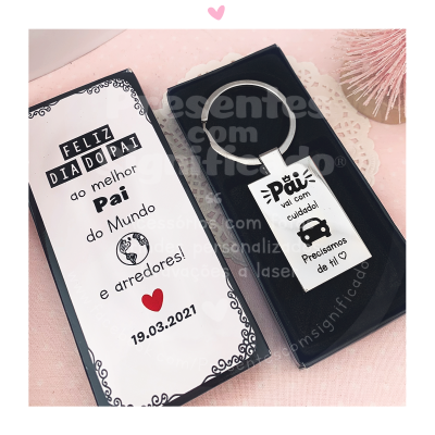Caixa branca com texto para o Dia do Pai e porta-chaves metálico com mensagem de cuidado num fundo cor-de-rosa.