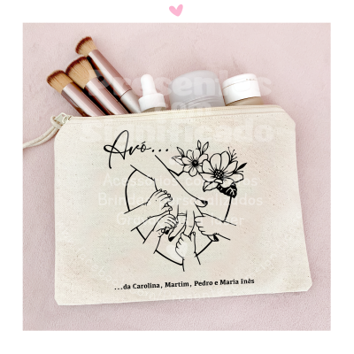 Bolsa de tecido bege com estampa de rosto e mãos de criança, contém pincéis de maquiagem e frascos, sobre fundo rosa.