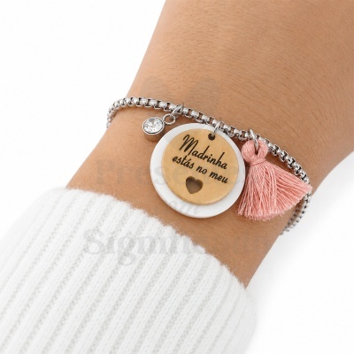 Pulseira prata com pendentes de disco em madeira e branco, borla rosa e cristal num pulso com manga branca de malha.
