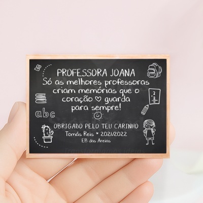 Placa de ardósia com texto em português e desenhos relacionados com escola, segurada por uma mão.