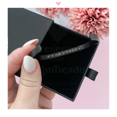 anel preto com números gravados sobre caixa preta e fundo com flores cor-de-rosa