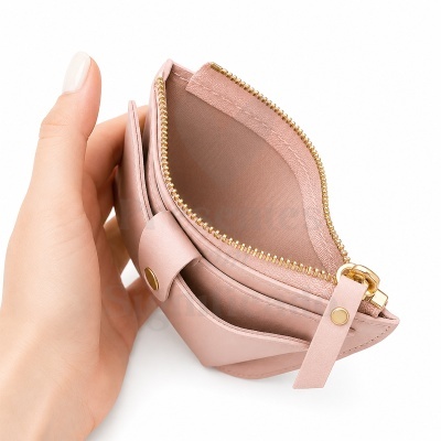Carteira rosa claro pequena com fecho dourado e botão, segurada por mão com unhas brancas