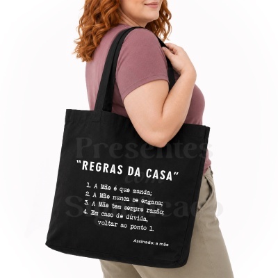 Mala preta de tecido com texto impresso branco, usada ao ombro de uma pessoa.