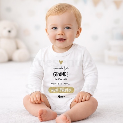 Bebé sorridente com body branco personalizado com texto em preto e dourado sentado em fundo branco desfocado.