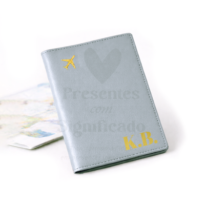 Capa de passaporte cinzenta com avião dourado e iniciais K.B.