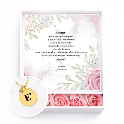 Caixa de presente branca com colar dourado com pendente redondo gravado com a letra E♥ e flores rosas artificiais.