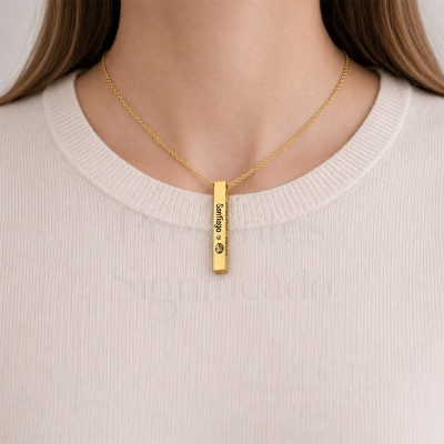 Colar dourado com pendente retangular gravado Santiago e coração em camisola bege.