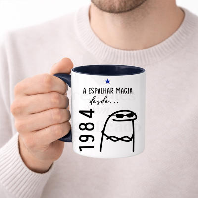 Caneca branca com pega azul escuro, texto e desenho preto, segurada por uma mão.