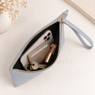 Mala clutch cinzenta com fecho dourado aberta, mostrando telemóvel, porta-cartões, baton e chaves no interior