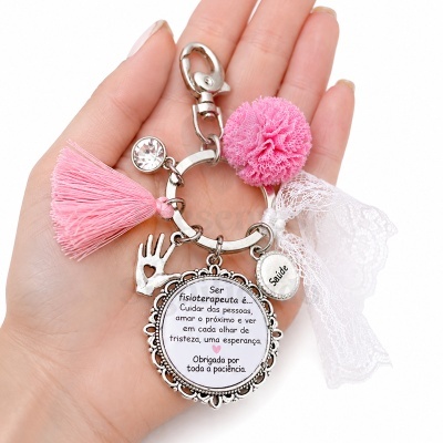 Chaveiro em metal com tassel rosa, pompom, renda branca e texto em português para fisioterapeuta