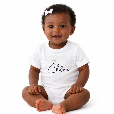 Bebé com body branco sentado em fundo branco, com a palavra Chloe e coroa dourada no corpo.