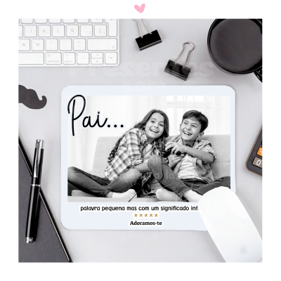 Tapete de rato com foto de crianças e texto, em secretária branca com teclado e caneca preta.