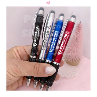 Quatro canetas táteis coloridas com texto branco seguradas por uma mão e fundo decorado em rosa