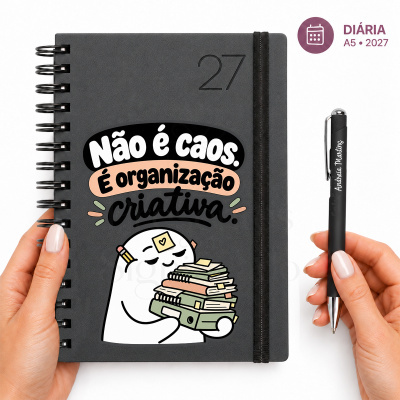 Caderno espiral cinza com texto e desenho colorido segurado por mão à esquerda e caneta preta segurada por mão à direita em fundo branco