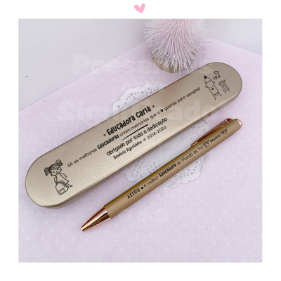 Estojo metálico cinza com caneta dourada e texto em português sobre educadores sobre fundo rosa claro com decoração branca.