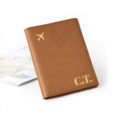 Capa de passaporte castanha com avião e iniciais douradas