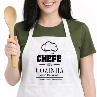 Pessoa de avental branco com texto CHEFE DESTA COZINHA Mamã Maria Inês e colher de madeira